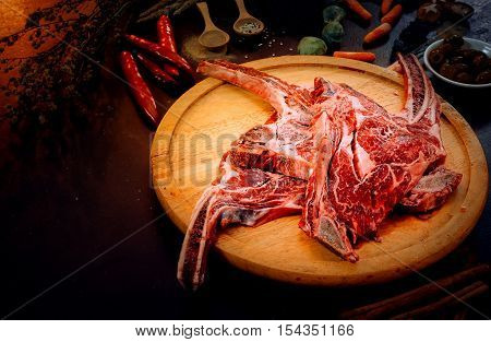 Raw triple tomahawk beef steak with ingredients for grilling with a spice rub fresh rosemary on black table.