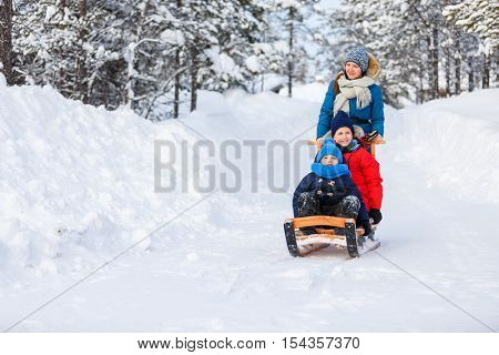 Beautiful family of mother and kids enjoying snowy winter day outdoors having fun sledging