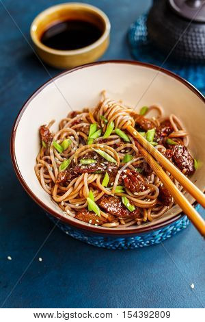 Fried noodles yakisoba with beef and sesame seeds in a bowl with chopsticks. Asian cuisine meal.