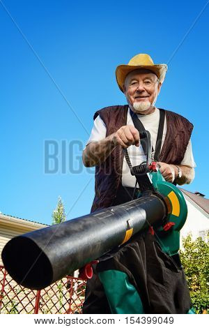 Autumn in a garden. Senior man removes fallen leaves in his garden using leaf blower.