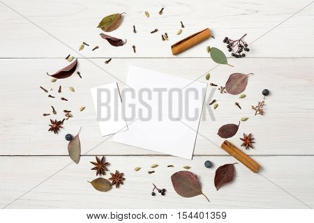 Autumn composition. Frame made of dried fall flowers and autumn leaves, also herbs as cinnamon, clove and sloe. Top view on white wood, flat lay, copy space on empty paper sheet