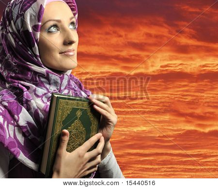 Adorabile ragazza musulmana tiene il libro sacro Corano, contro il cielo rosso