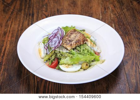Nicoise salad in a plate on the table. In the plate is tuna eggs asparagus lettuce olives onions tomatoes spices