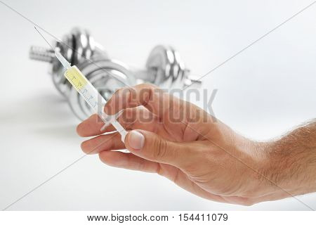 Male hand holding syringe and dumbbells in background
