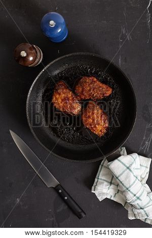 Korean style glazed pork chops on black background. Sticky citrus caramelized sauce with oranges and mint leaves. Salt, pepper, knife near pan with chops.