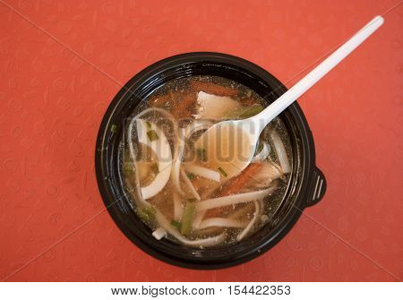 Tomyam soup in fast food wih plastic spoon top view on red background.