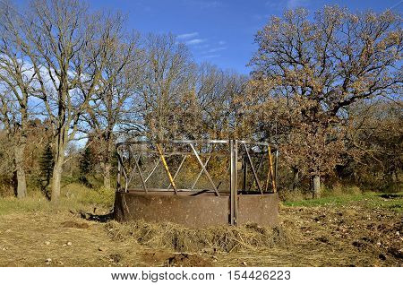 Old cattle feeder with  hay strewn on the ground in a pasture or feedlot