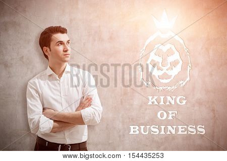 Young man in white shirt standing near concrete wall with king of business sketch on it. Concept of true leader. Toned image