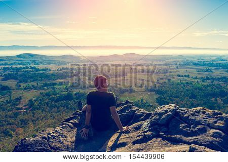 Young Man In Green Sportswear Is Sitting On Cliff's Edge