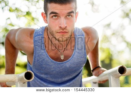 Closeup portrait of sports man doing pull-ups on parallel crossbars on nature