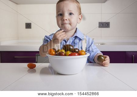 Baby boy tasting ripe colorful cherry tomatoe. Education on healthy nutrition for children concept
