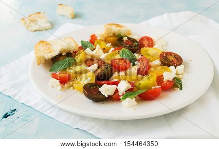 Summer heirloom tomato salad with fresh feta cheese on white plate on blue background selective focus horizontal