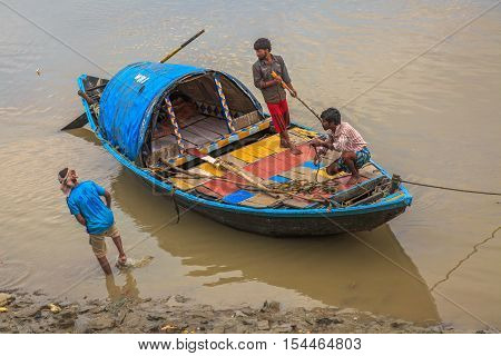KOLKATA, INDIA - OCTOBER 31, 2016: Wooden country boat stuck in mud at low tide on the Ganges river near Outram ghat, Kolkata. Fishermen trying to get the boat offshore.