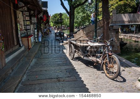 ZHUJIAJIAO CHINA - AUGUST 30 2016: Rusty three wheeled freight electric bike parked on canal embankment of ancient water town in Zhujiajiao China on August 30 2016.