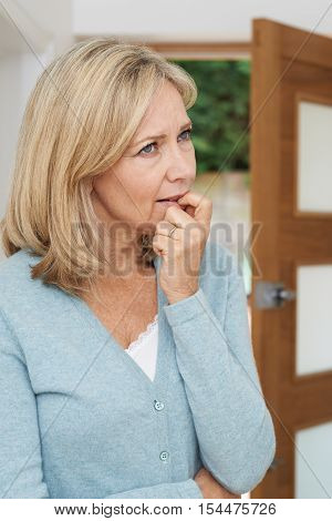 Sad Mature Woman Suffering From Agoraphobia Looking Out Of Open Door