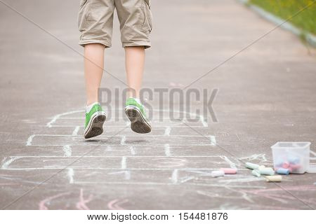 Closeup of boy's legs and hopscotch drawn on asphalt. Child playing hopscotch on playground outdoors on a sunny day. outdoor activities for children.