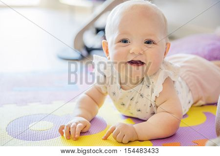 Happy baby girl with blue eyes playing on the floor with toys on a playmat. A cute young child plays and smiles.