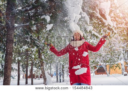 The girl is under the snow pouring from the tree cheerful mood and joy the first snow in winter park. Hands raised up towards the snow.