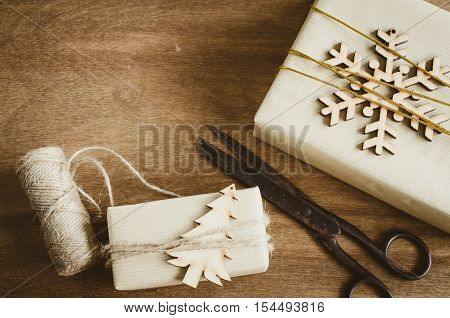 Kraft Boxes with Gifts Decorated with Wooden Snowflake Christmas Tree and Jute on Wooden Background. Old Vintage Scissors. Christmas in Rustic Style. View from above with copy space.