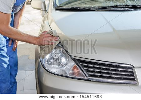 The worker polishes optics of headlights of the car to restore gloss and transparency