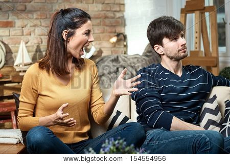 Young couple arguing at home, woman shouting, man turning away head.
