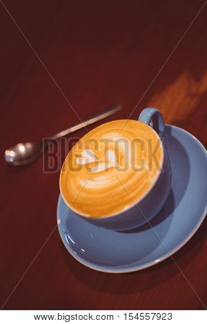 Close-up of delicious fresh latte art in blue cup on saucer with spoon