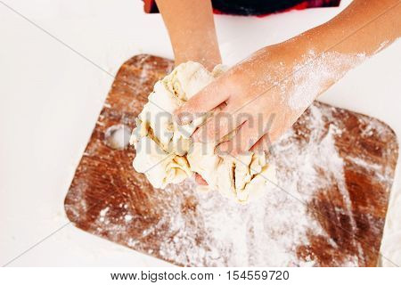 Kid hands with dough close-up. Top view on little baker kneading raw pastry above wooden cutting board. Homemade bakery, children culinary, sweets making concept