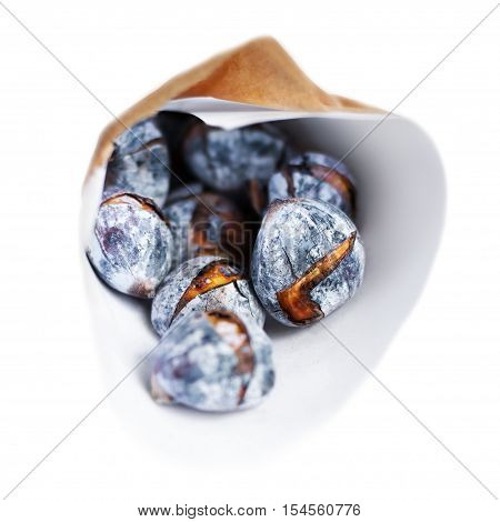 Roasted chestnuts in a craft paper bag isolated on white background close up. Heap of grilled edible chestnut
