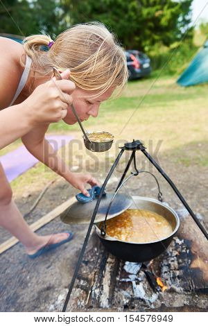 Woman is tasting the soup cooked on the campfire in a hike