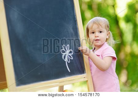 Adorable toddler drawing with a chalk on a blackboard