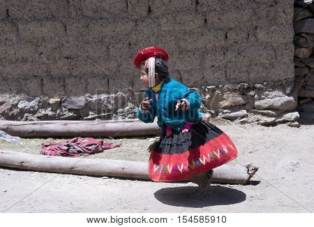 Peruvian girl running dressed in colourful traditional handmade outfit. October 21 2012 - Patachancha Cuzco Peru