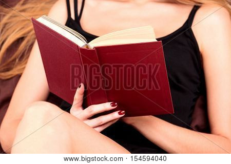 close up of young woman reading book in bed 