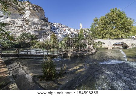 Alcala del Jucar Spain - October 29 2016: Small wooden bridge over the river Jucar located in the central part of the town the fund for the Church of San Andres styles late Gothic and Neoclassic take in Alcala of the Jucar Albacete province Spain