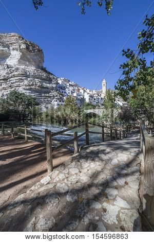 Alcala del Jucar Spain - October 29 2016: Small wooden bridge over the river Jucar located in the central part of the town the fund for the Church of San Andres styles late Gothic and Neoclassic take in Alcala of the Jucar Albacete province Spain