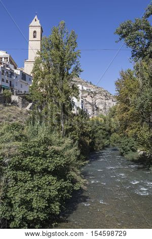 Alcala del Jucar Spain - October 29 2016: Clear waters of the river Jucar on the Roman bridge to the left the Church of San Andres of styles late and neoclassic Gothic take in Alcala of the Jucar Albacete province Spain