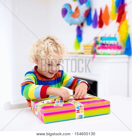 Child celebrating third birthday. Little boy opening presents and holding balloons in decorated room. Birthday party for kids.