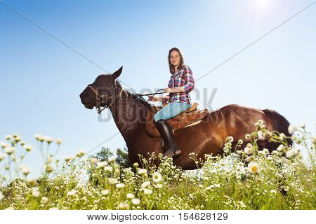 Side view portrait of beautiful girl riding bay horse in countryside