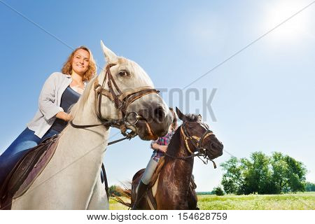 Close-up portrait of two happy female equestrians riding beautiful purebred horses at flowery meadows