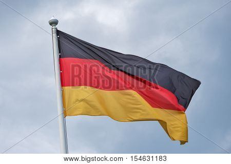 The flag of Germany flutters on wind against the background of gray clouds.