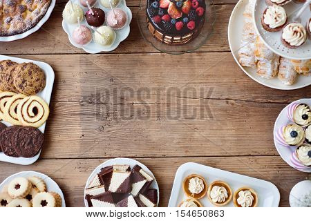 Table with cake, pie, cupcakes, tarts and cakepops. Frame composition. Studio shot on brown wooden background. Copy space. Flat lay.