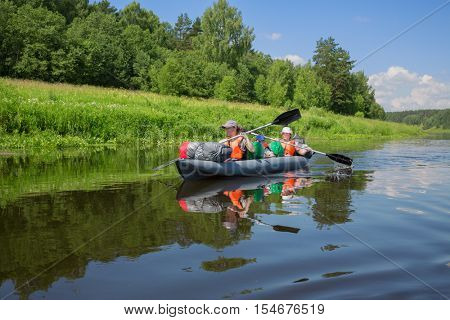Two adults and boy in life jackets sail on inflatable boats during hike at summer