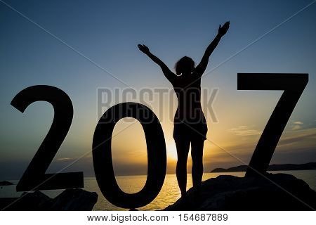 Happy new 2017 year card. A girl standing on a rocky shore watching the sunset standing as a part of 2017 sign