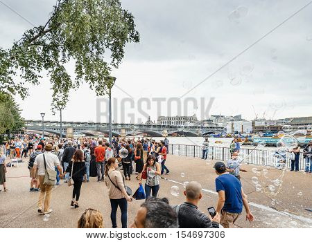 LONDON UNITED KINGDOM - JUL 9 2016: Group of people having fun with soap bubbles next to MOMA museum next to Thames riverbank - best adventure and vacancy in United Kingdom