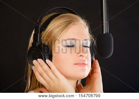 Music passion stage-fright concept. Blonde young woman singing to microphone and wearing big headphones on her head performing songs in studio.