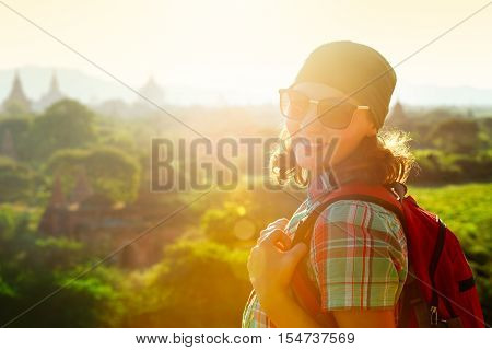 Portrait a smiling young woman traveler with a backpack on the background of the sunset over the ancient temples. Traveling freedom and active lifestyle concept.