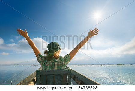Happy carefree woman in travels by boat . Traveller woman in sunshine glow of sun with arms outspread and face raised in sky enjoying open spaces on lake serenity in nature.