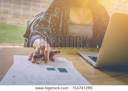 Business woman hand holding pen with laptop computer and working Finance Report Statistic. vintage effect.