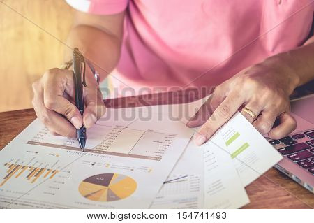 Business man hand holding pen point graph chart documen and use computer laptop in office.
