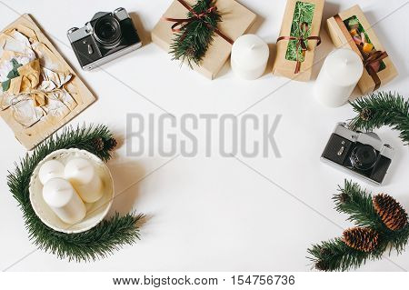 Christmas and New Year background with vintage film camera, white candles, tray, gifts, spruce cones and braches on white background. Top view, flat lay