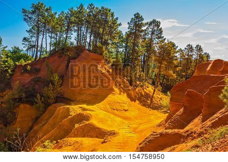 Unique red and orange hills in the province of Roussillon, France. Coniferous forests create a beautiful contrast with the color of ocher